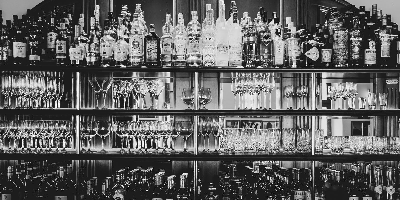 Schwarz-Weiß-Foto einer Bar: Regale voller Flaschen und Reihen von Gläsern.